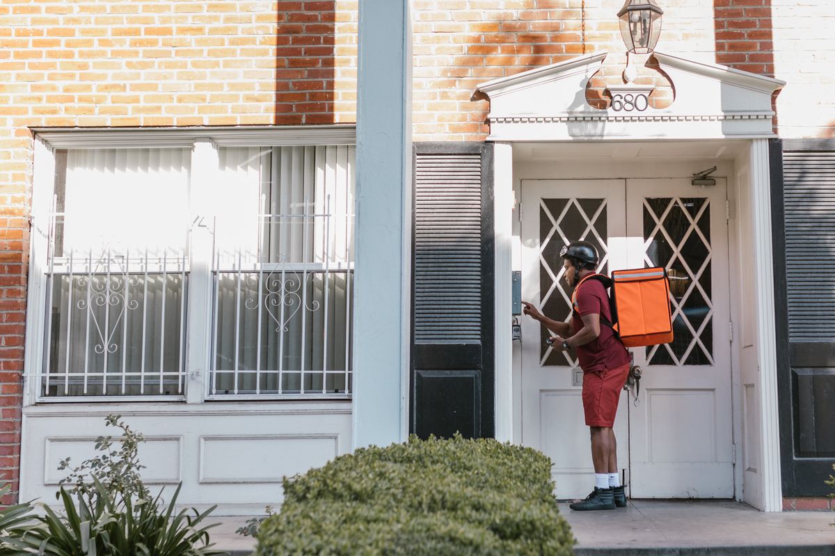 Delivery driver pressing a video doorbell at a house entrance